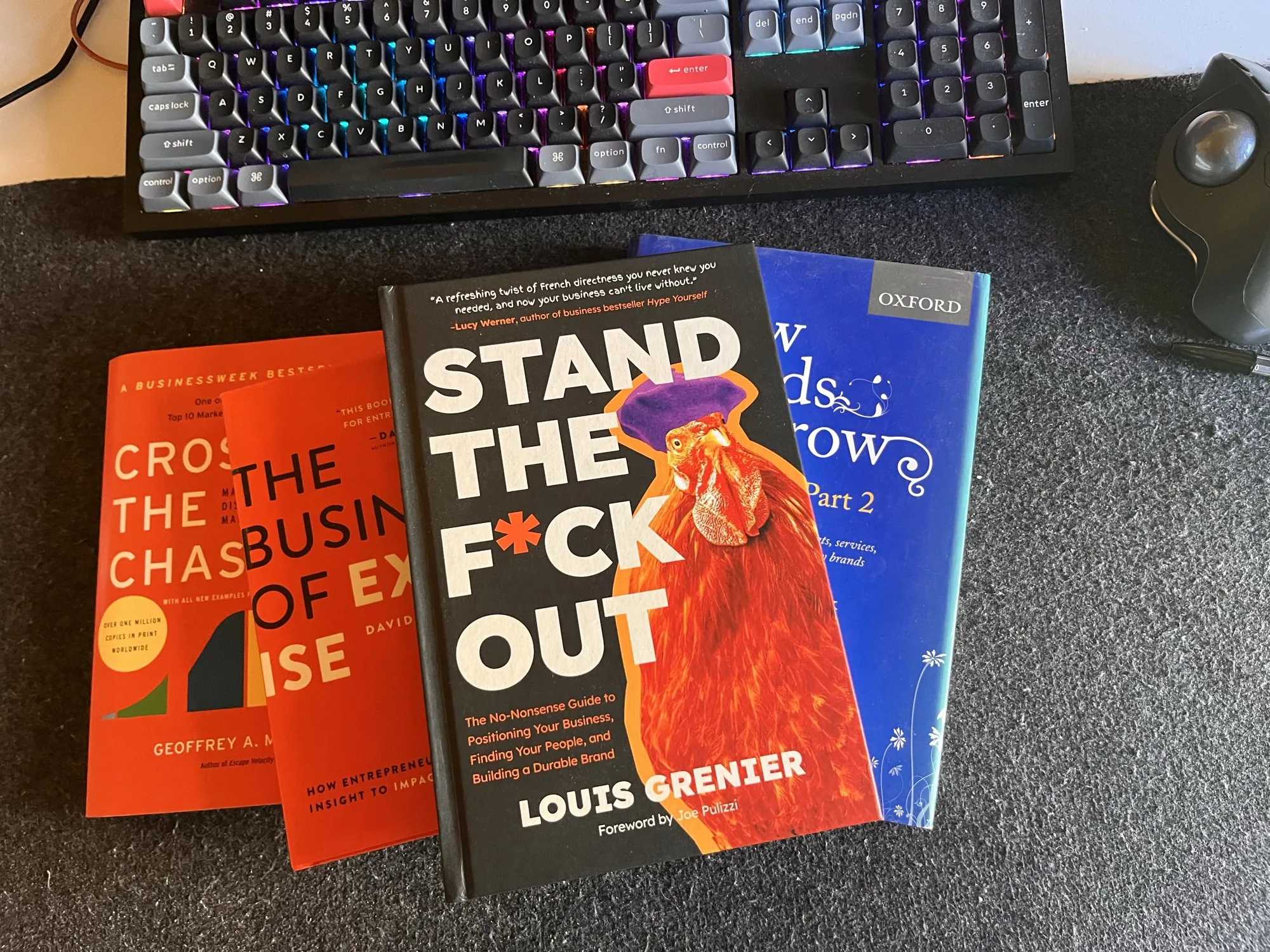 Four B2B positioning books on a desk next to a keyboard: Crossing the Chasm, The Business of Expertise, Stand The F*ck Out, and How Brands Grow Part 2