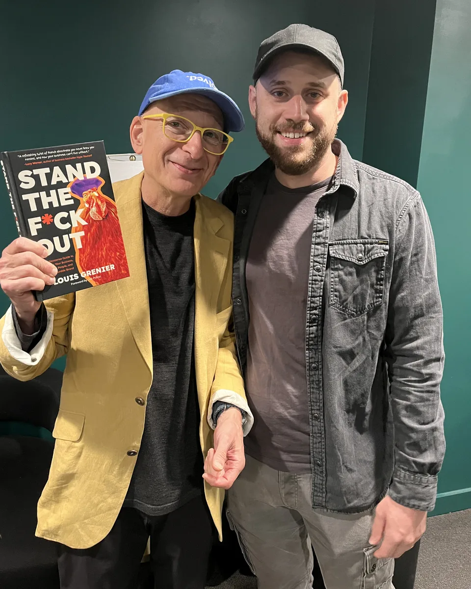 Louis Grenier backstage with Seth Godin, who is holding up a copy of Stand The F*ck Out, at Exit Five's Drive 2026.